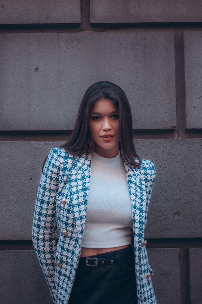 Fashionable woman in a blue jacket poses confidently by a concrete wall.