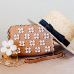 Chic ensemble featuring a floral handbag, straw hat, and perfume, perfect for summer fashion.