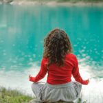 Person meditating calmly beside water