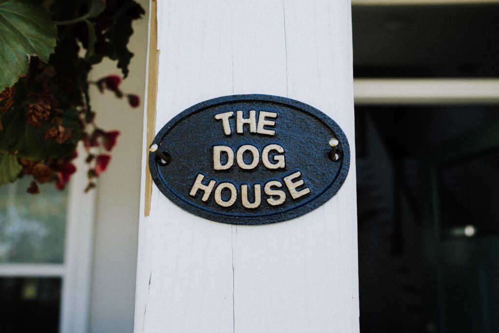 Oval house name sign reading The Dog House on a white post