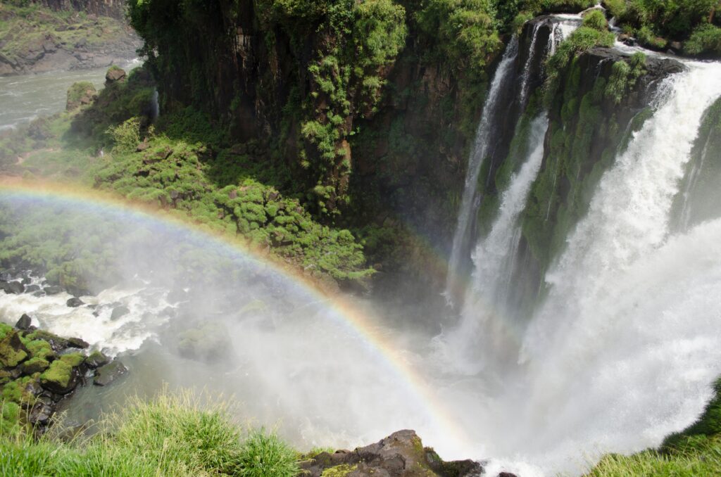 Stunning view of a rainbow against the backdrop of Iguazu Falls and lush greenery.