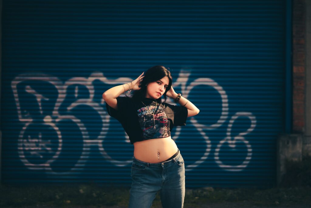 Trendy young woman in casual outfit posing in front of a graffiti-covered wall, showcasing urban fashion style.