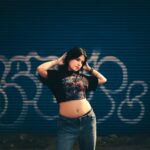 Trendy young woman in casual outfit posing in front of a graffiti-covered wall, showcasing urban fashion style.