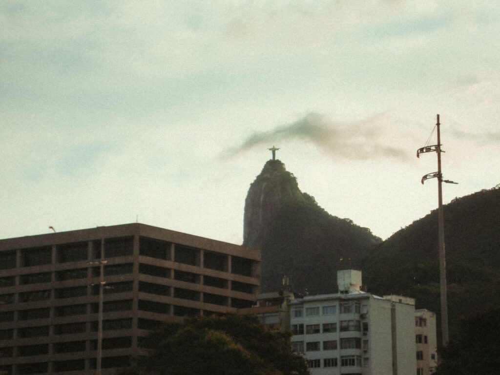 Christ the Redeemer statue on Corcovado Mountain with Rio de Janeiro cityscape under a cloudy sky.