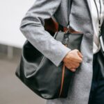 Crop faceless female entrepreneur in stylish classy outfit with bag and name tag walking on city street
