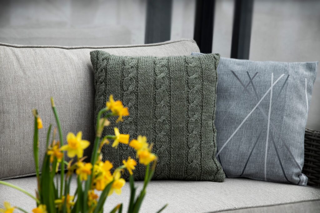 Sofa close-up with a green knitted cushion and yellow flowers